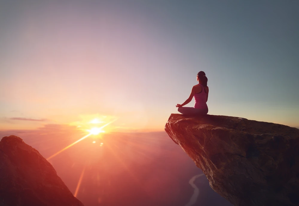 Vrouw mediteert in kleermakerzit op klif in de bergen bij zonsopgang of zonsondergang.
