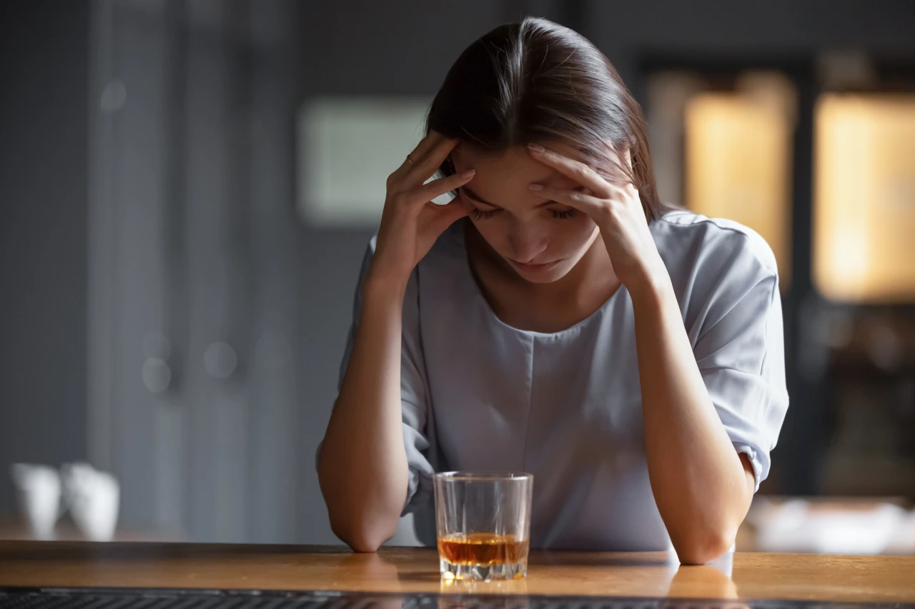 Vrouw met glas alcohol steunt hoofd in handen en is voorbeeld van hoe je verslaving herkent. 